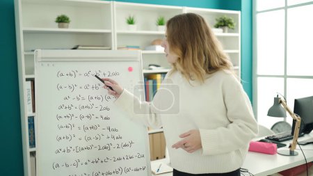 Téléchargez les photos : Jeune enseignante blonde expliquant l'exercice de mathématiques dans une salle de classe universitaire - en image libre de droit