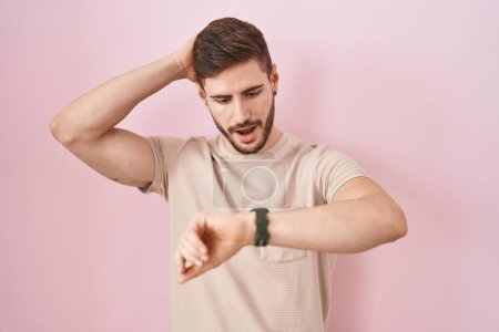 Téléchargez les photos : Homme hispanique avec barbe debout sur fond rose regardant le temps de la montre inquiet, peur de se faire tard - en image libre de droit