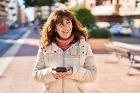 Foto de Mujer de mediana edad sonriendo confiado usando teléfono inteligente en el parque - Imagen libre de derechos