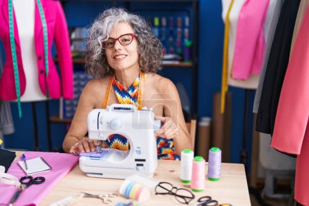 Photo for Middle age grey-haired woman tailor smiling confident using sewing machine at sewing studio - Royalty Free Image