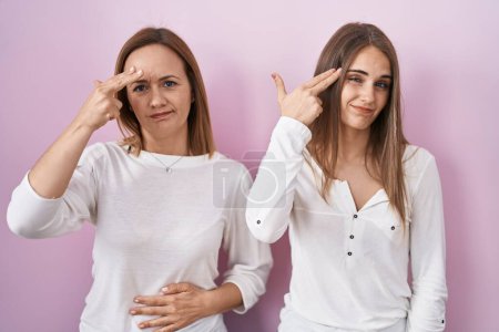 Photo for Middle age mother and young daughter standing over pink background shooting and killing oneself pointing hand and fingers to head like gun, suicide gesture. - Royalty Free Image