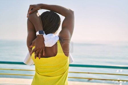 Photo for African american woman wearing sportswear stretching arm at seaside - Royalty Free Image