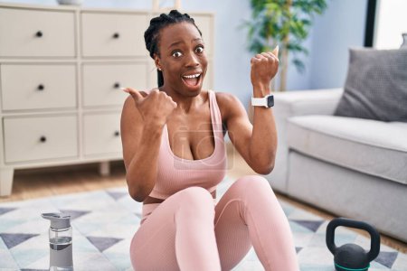 Photo for Beautiful black woman using smart watch training at home pointing thumb up to the side smiling happy with open mouth - Royalty Free Image