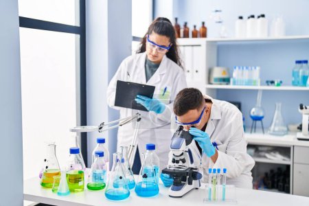 Téléchargez les photos : Man and woman wearing scientist uniform using microscope write on document at laboratory - en image libre de droit