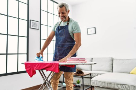Photo for Middle age grey-haired man smiling confident ironing clothes at home - Royalty Free Image