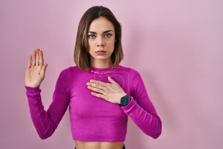 Téléchargez les photos : Hispanic woman standing over pink background swearing with hand on chest and open palm, making a loyalty promise oath - en image libre de droit