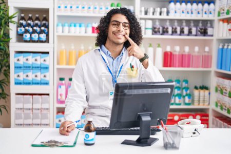 Photo for Hispanic man with curly hair working at pharmacy drugstore smiling cheerful showing and pointing with fingers teeth and mouth. dental health concept. - Royalty Free Image