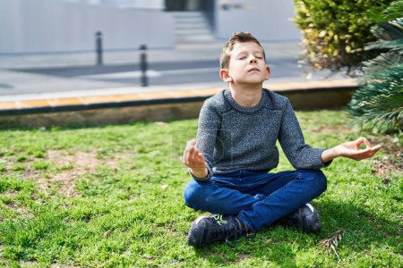 Téléchargez les photos : Enfant blond faisant des exercices de yoga assis sur l'herbe au parc - en image libre de droit