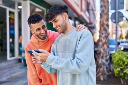 Foto de Dos parejas de hombres abrazándose usando un teléfono inteligente en la calle - Imagen libre de derechos