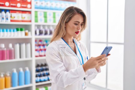 Téléchargez les photos : Jeune belle pharmacienne hispanique utilisant un smartphone travaillant à la pharmacie - en image libre de droit