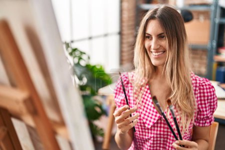 Téléchargez les photos : Young woman artist smiling confident holding paintbrushes at art studio - en image libre de droit
