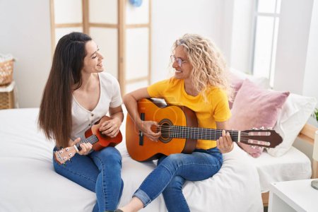 Photo for Two women mother and daughter playing classical guitar and ukulele at bedroom - Royalty Free Image