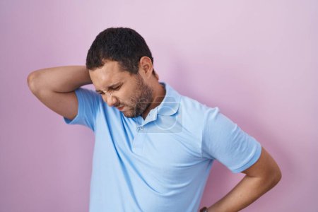Foto de Hombre hispano de pie sobre fondo rosa sufriendo de dolor de cuello lesión, tocando el cuello con la mano, dolor muscular - Imagen libre de derechos