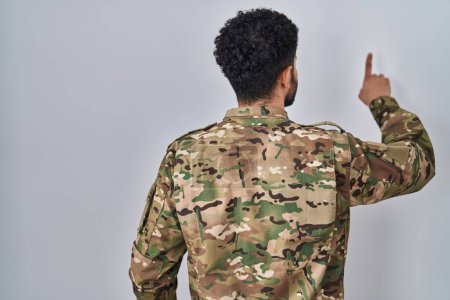 Foto de Hombre árabe vistiendo uniforme camuflaje ejército posando hacia atrás apuntando hacia adelante con la mano del dedo - Imagen libre de derechos