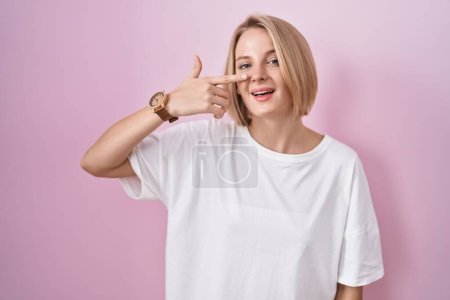 Téléchargez les photos : Jeune femme caucasienne debout sur fond rose pointant avec le doigt de la main sur le visage et le nez, souriant gai. concept de beauté - en image libre de droit