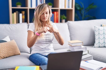 Foto de Mujer rubia joven estudiando el uso de ordenador portátil en casa rechazo expresión cruzando los dedos haciendo signo negativo - Imagen libre de derechos