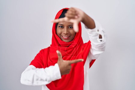 Téléchargez les photos : Jeune femme arabe portant l'écharpe traditionnelle islamique hijab souriant faisant cadre avec les mains et les doigts avec le visage heureux. concept de créativité et photographie. - en image libre de droit