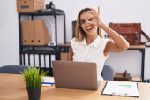 Young blonde woman working at the office wearing glasses smiling happy doing ok sign with hand on eye looking through fingers  Poster #658046574