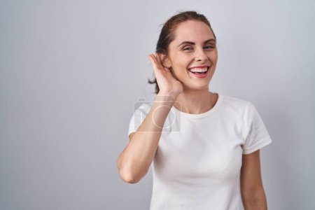 Photo for Beautiful brunette woman standing over isolated background smiling with hand over ear listening an hearing to rumor or gossip. deafness concept. - Royalty Free Image