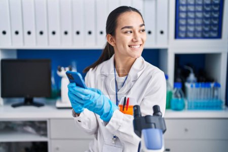 Photo for Young hispanic woman scientist using smartphone working at laboratory - Royalty Free Image