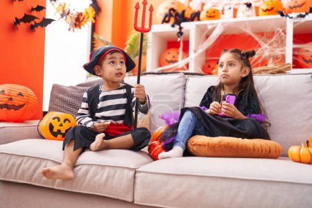 Photo for Adorable boy and girl having halloween party sitting on sofa at home - Royalty Free Image