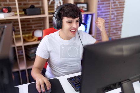Téléchargez les photos : Non binaire homme streamer jouer jeu vidéo avec l'expression gagnante à la salle de jeu - en image libre de droit