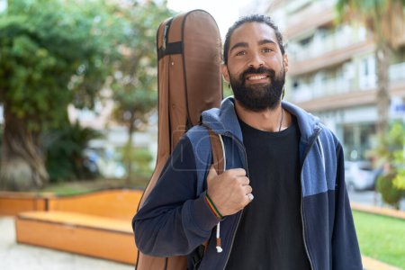 Téléchargez les photos : Young hispanic man musician smiling confident holding guitar case at park - en image libre de droit