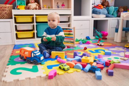 Foto de Adorable chico caucásico jugando con juguetes sentados en el suelo en el jardín de infantes - Imagen libre de derechos