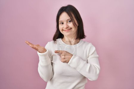 Téléchargez les photos : Femme avec le syndrome du duvet debout sur fond rose étonné et souriant à la caméra tout en présentant avec la main et pointant du doigt. - en image libre de droit