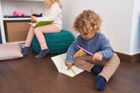 Photo for Adorable boy and girl students sitting on floor drawing on notebook at classroom - Royalty Free Image