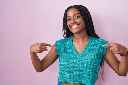 Photo for Young african american with braids standing over pink background looking confident with smile on face, pointing oneself with fingers proud and happy. - Royalty Free Image