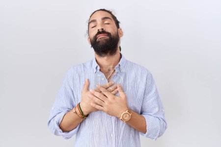 Foto de Hombre hispano con barba vistiendo camisa casual sonriendo con las manos en el pecho con los ojos cerrados y gesto agradecido en la cara. concepto de salud. - Imagen libre de derechos