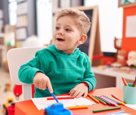 Photo for Adorable caucasian boy preschool student sitting on table drawing on notebook at kindergarten - Royalty Free Image