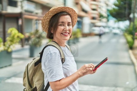 Téléchargez les photos : Femme d'âge moyen touriste souriant confiant en utilisant smartphone à la rue - en image libre de droit