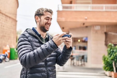 Téléchargez les photos : Jeune homme souriant confiant jouer jeu vidéo à la rue - en image libre de droit