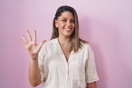 Photo for Blonde woman standing over pink background showing and pointing up with fingers number five while smiling confident and happy. - Royalty Free Image