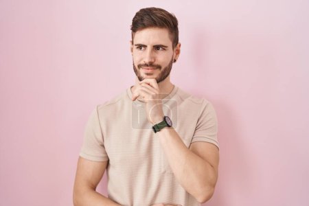 Photo for Hispanic man with beard standing over pink background with hand on chin thinking about question, pensive expression. smiling and thoughtful face. doubt concept. - Royalty Free Image
