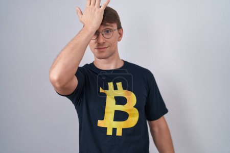 Téléchargez les photos : Homme blond caucasien portant Bitcoin t-shirt surpris avec la main sur la tête pour erreur, rappelez-vous erreur. oublié, mauvais concept de mémoire. - en image libre de droit
