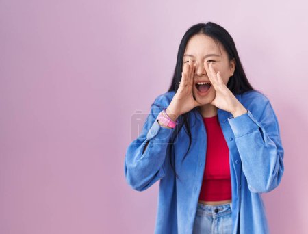 Téléchargez les photos : Jeune femme asiatique debout sur fond rose criant en colère à haute voix avec les mains sur la bouche - en image libre de droit