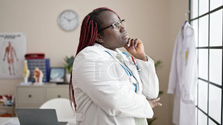 Téléchargez les photos : Femme africaine avec médecin cheveux tressés regardant par la fenêtre debout à la clinique - en image libre de droit