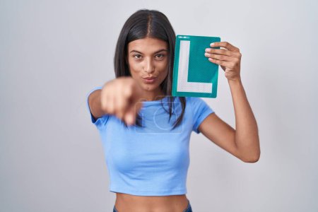 Photo for Brunette young woman holding l sign for new driver pointing with finger to the camera and to you, confident gesture looking serious - Royalty Free Image