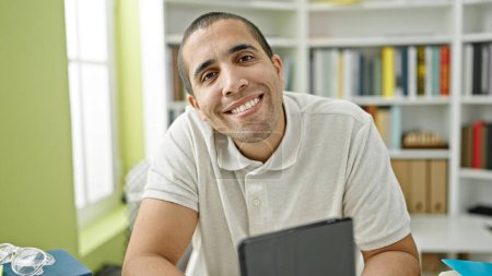 Photo for Young hispanic man student sitting smiling confident at library university - Royalty Free Image