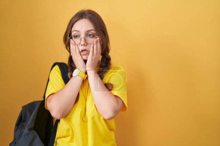 Téléchargez les photos : Jeune femme caucasienne portant sac à dos étudiant sur fond jaune mains fatiguées couvrant le visage, la dépression et la tristesse, contrarié et irrité par le problème - en image libre de droit