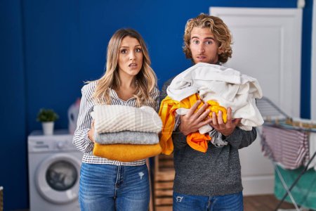 Photo for Young couple doing laundry clueless and confused expression. doubt concept. - Royalty Free Image