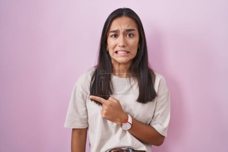 Foto de Mujer hispana joven de pie sobre fondo rosa señalando a un lado preocupado y nervioso con el dedo índice, preocupado y expresión sorprendida - Imagen libre de derechos