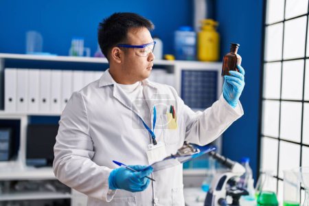 Photo for Young chinese man wearing scientist uniform reading clipboard at laboratory - Royalty Free Image