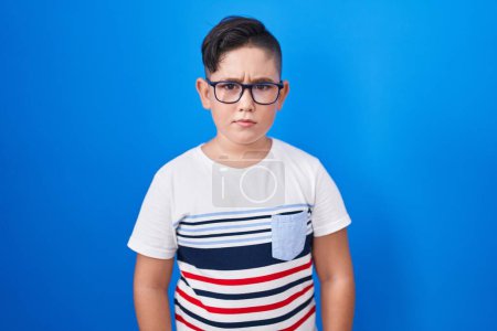 Photo for Young hispanic kid standing over blue background skeptic and nervous, frowning upset because of problem. negative person. - Royalty Free Image
