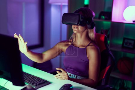 Téléchargez les photos : Young blonde woman streamer playing video game using virtual reality glasses at gaming room - en image libre de droit
