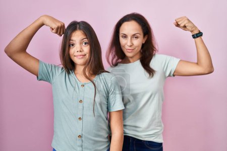 Téléchargez les photos : Jeune mère et fille debout sur fond rose personne forte montrant muscle du bras, confiant et fier de la puissance - en image libre de droit