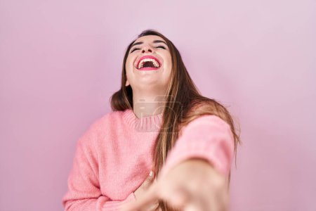 Photo for Young hispanic woman standing over pink background laughing at you, pointing finger to the camera with hand over body, shame expression - Royalty Free Image